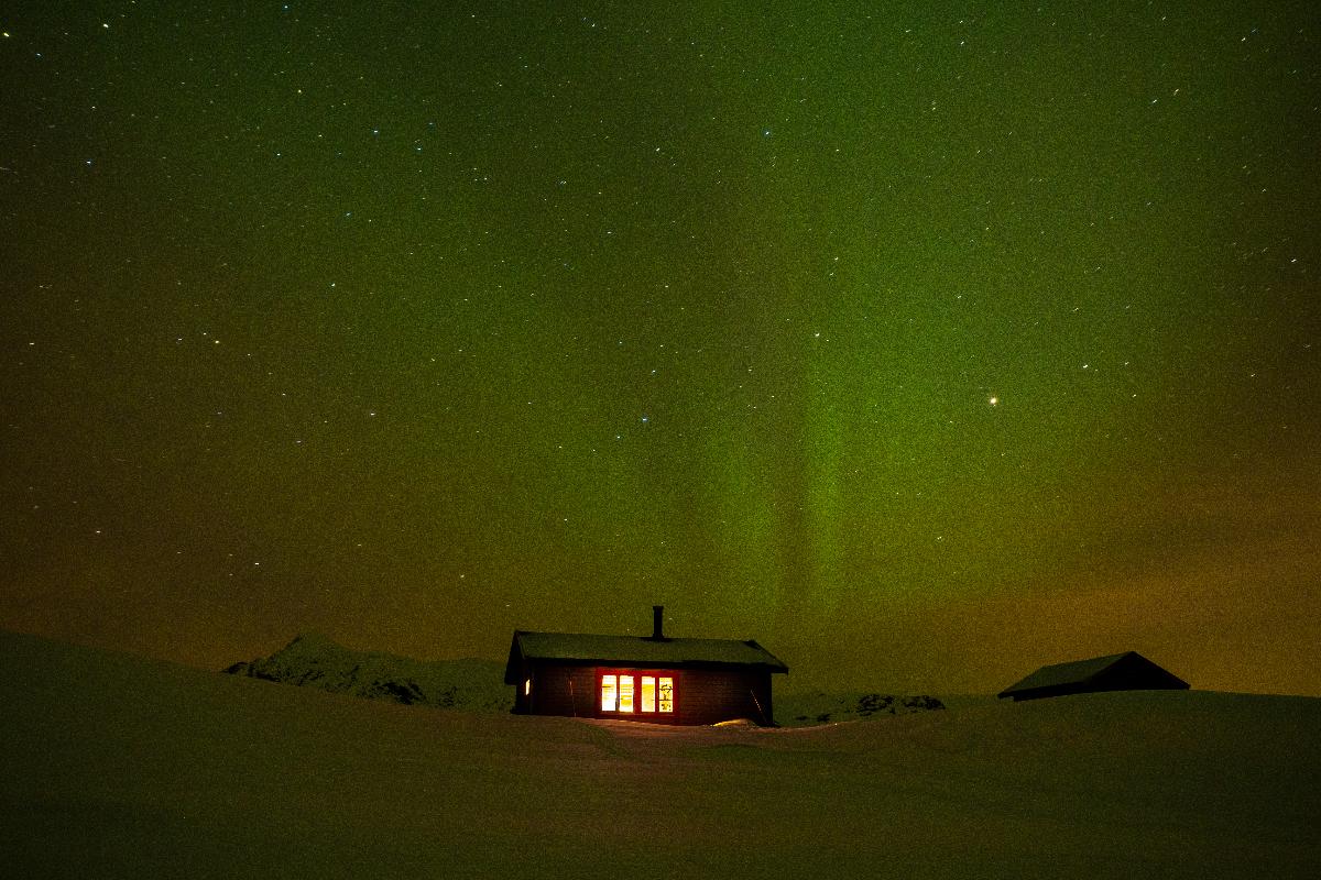 Under en stjernehimmel ligger en hytte i snølandskapet. 